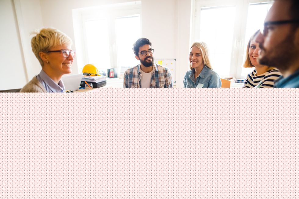 Two men and women sit in a semi-circle facing a woman with blond short hair. They're all listening and smiling.